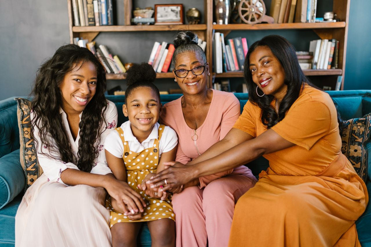 Smiling African American women of different generations sitting together on a cozy couch indoors.